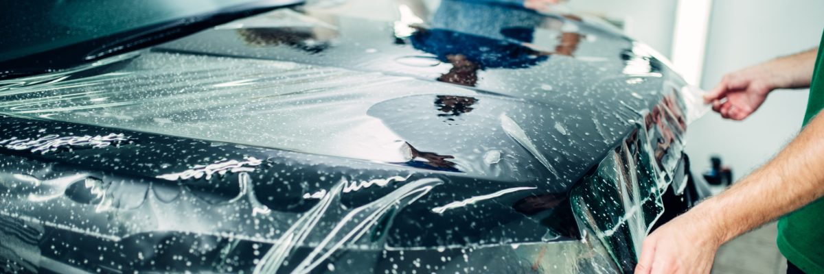 Transparent film, car paint protection installation process. Protect against chips and scratches. Workers wraps hood in protective coating