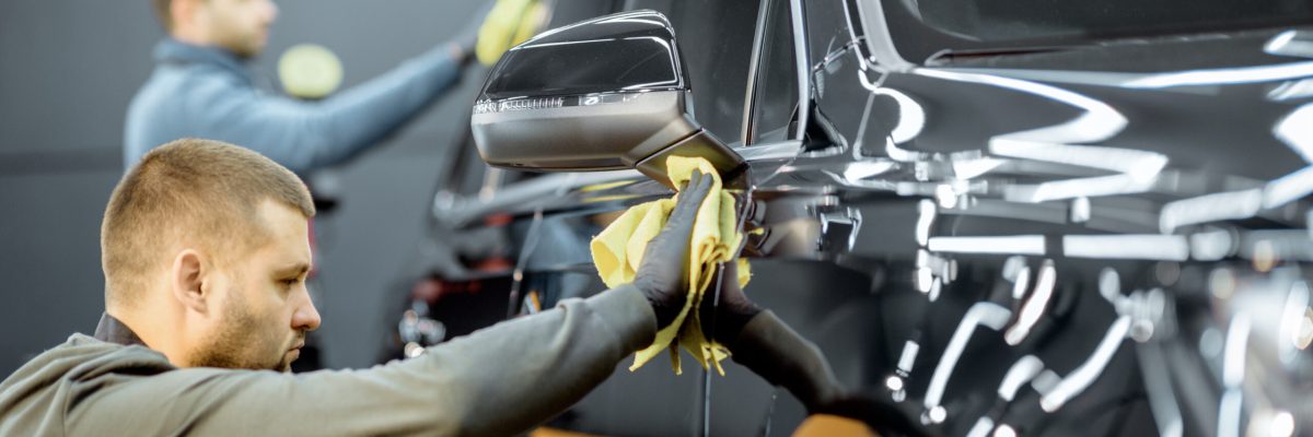 Car service workers wiping vehicle body with microfiber, examining glossy coating after the polishing procedure. Professional car detailing and maintenance concept